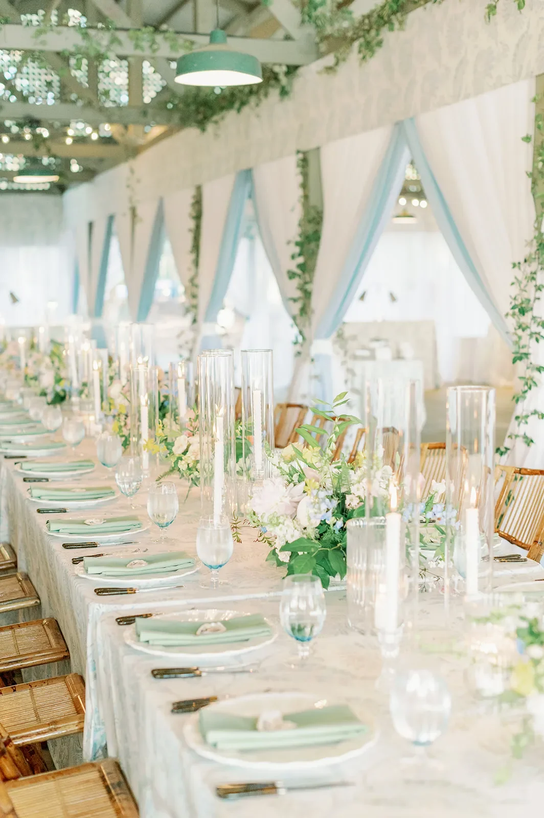 Long wedding table with pale green napkins, white flowers, and glass candle holders