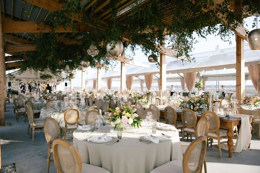 Large tented reception with round tables, upholstered dining chairs and floral centerpieces