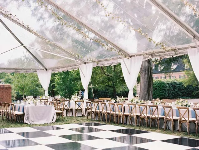 black-and-white floor beneath hanging lights and greenery at an outdoor wedding reception.