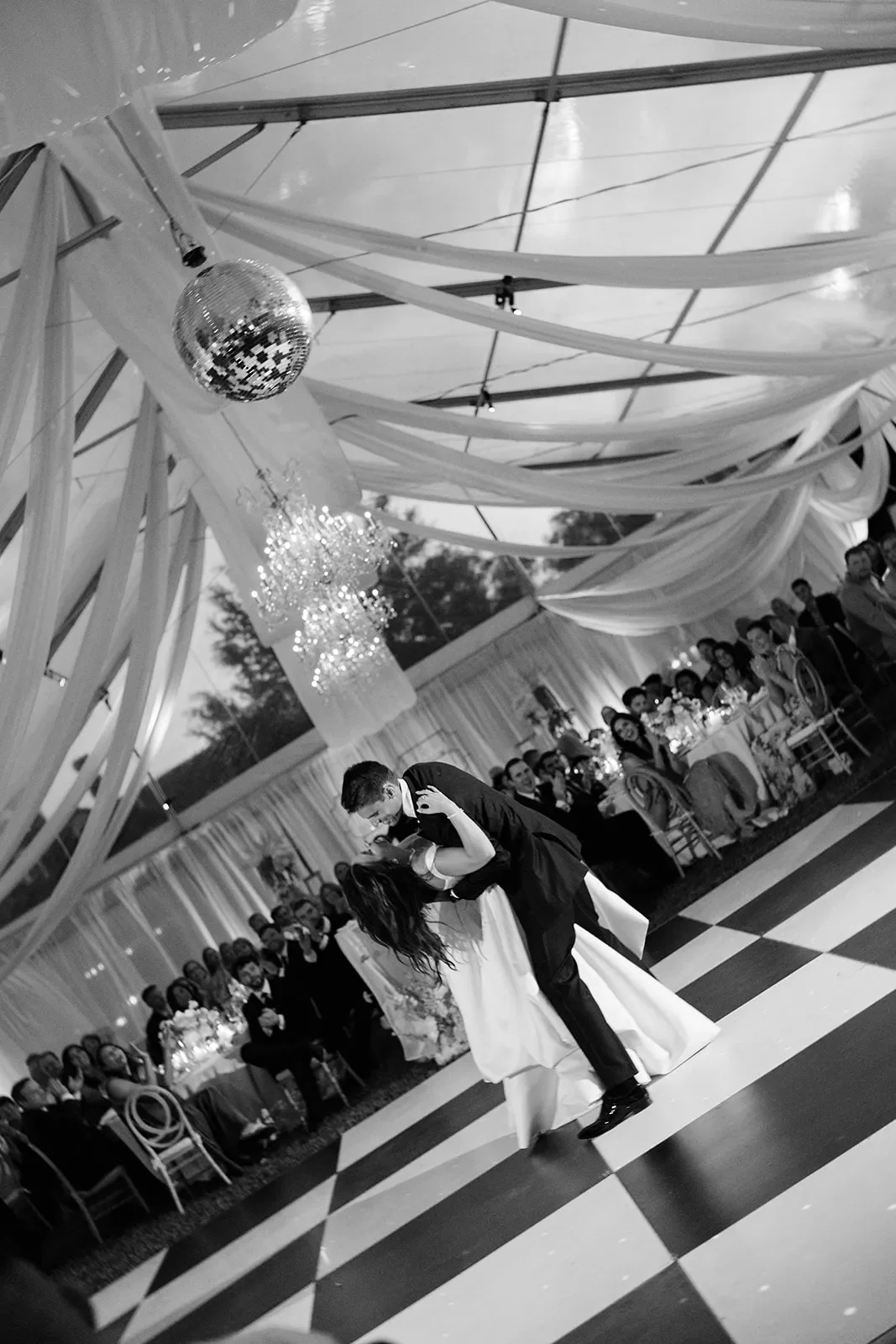 Newlyweds dancing beneath a disco ball inside a draped wedding tent