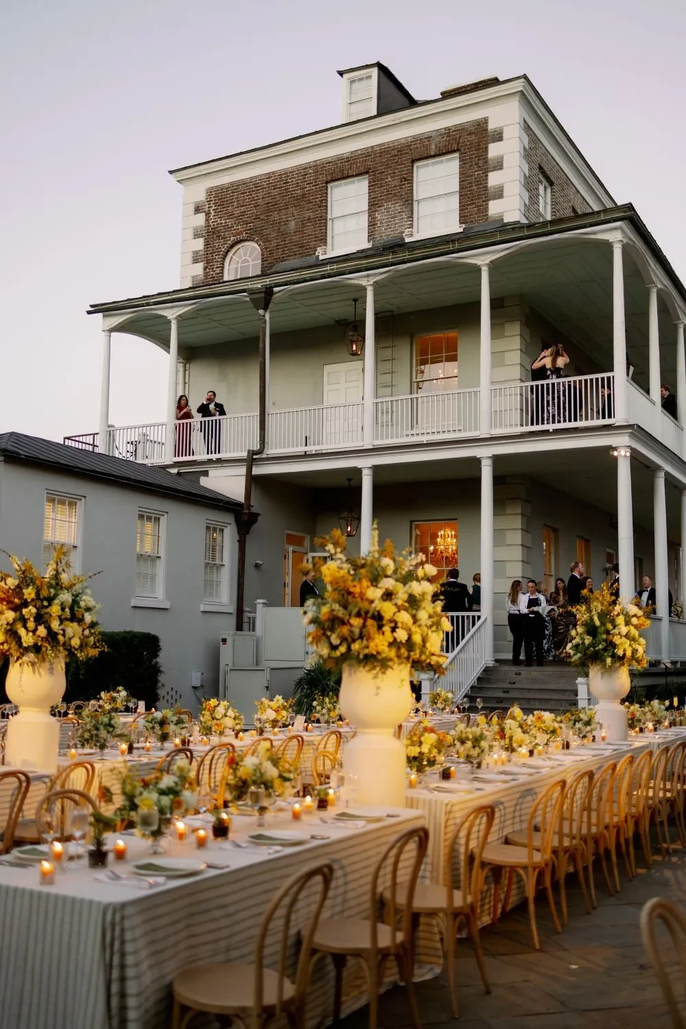Long outdoor wedding table with gold chairs and tall floral arrangements outside a historic Charleston home