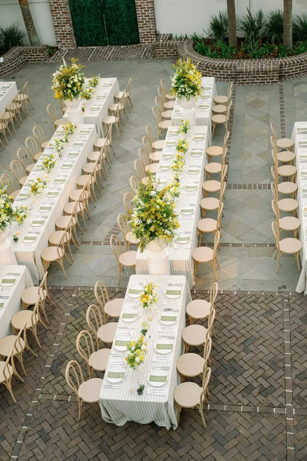 Long Charleston wedding tables with striped linens, yellow flowers, and light wood chairs Long Charleston wedding tables with striped linens, yellow flowers, and light wood chairs