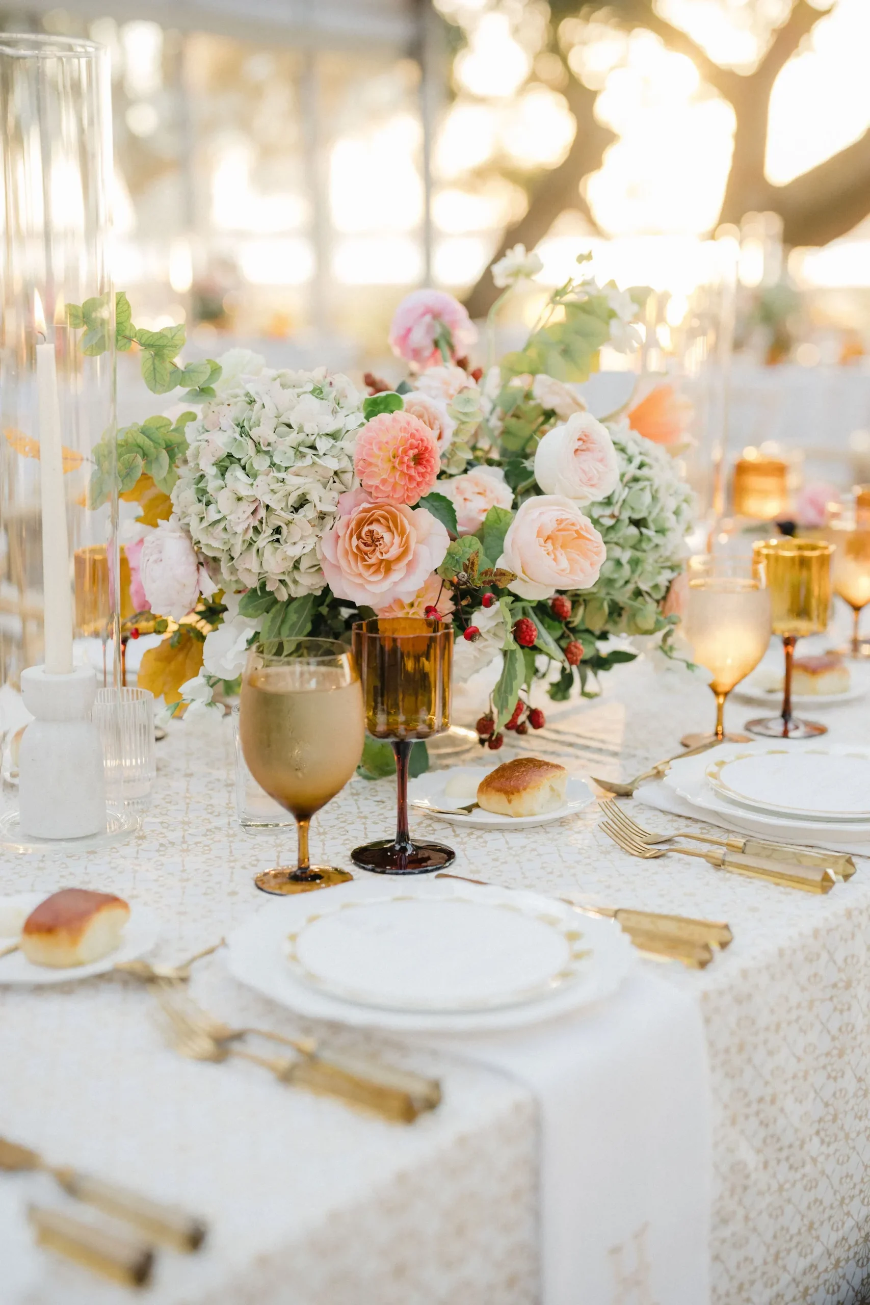 Fall wedding table with patterned ivory linen, peach flowers, amber glasses, and gold flatware
