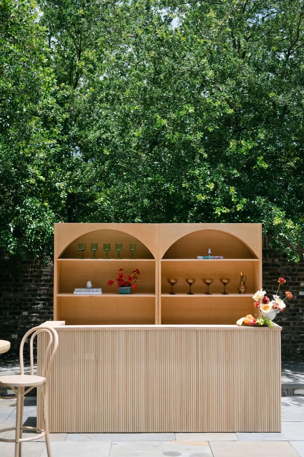 Natural wood bar with matching arched backbar shelves and colorful glassware outdoors