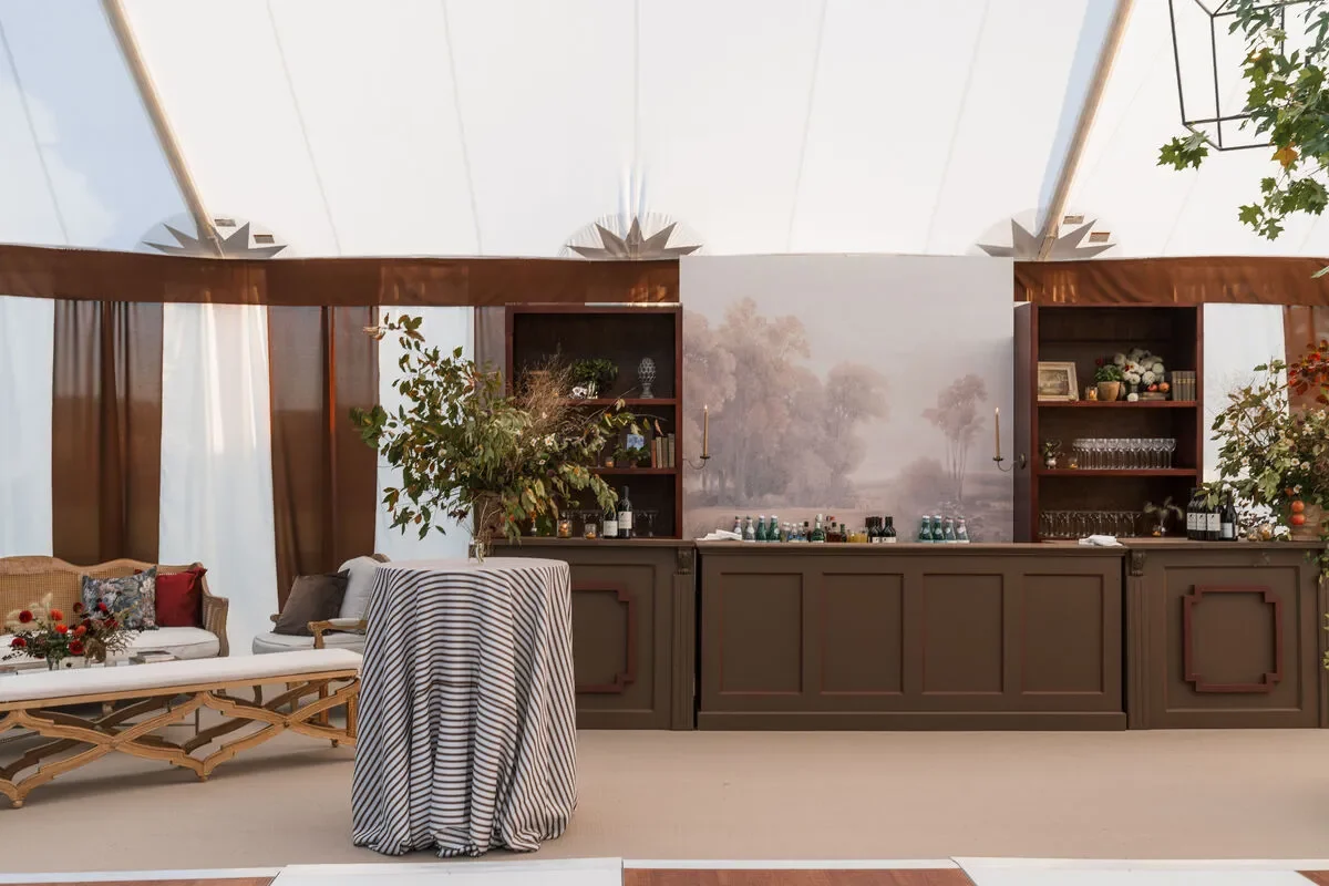 Brown paneled reception bar with shelving, lounge seating, and a striped cocktail table