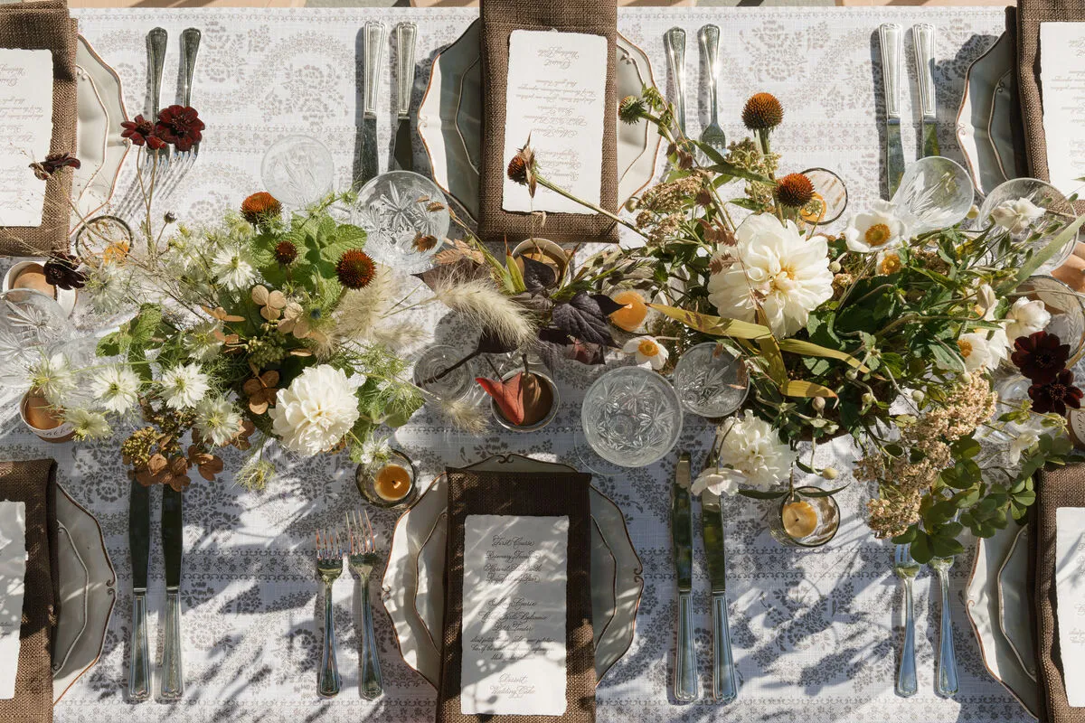 Overhead formal place settings with patterned linen, florals, glassware, and menu cards