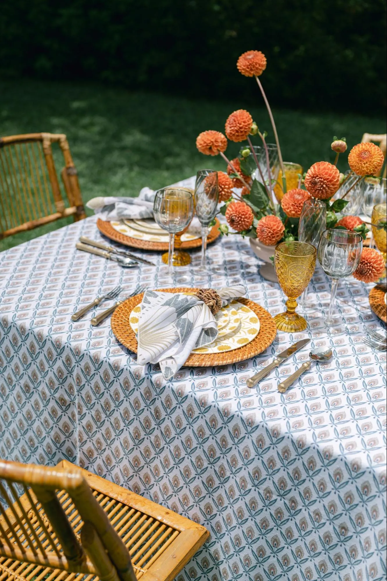 Fall tablescape with patterned linen, amber glassware, woven chargers, and orange florals