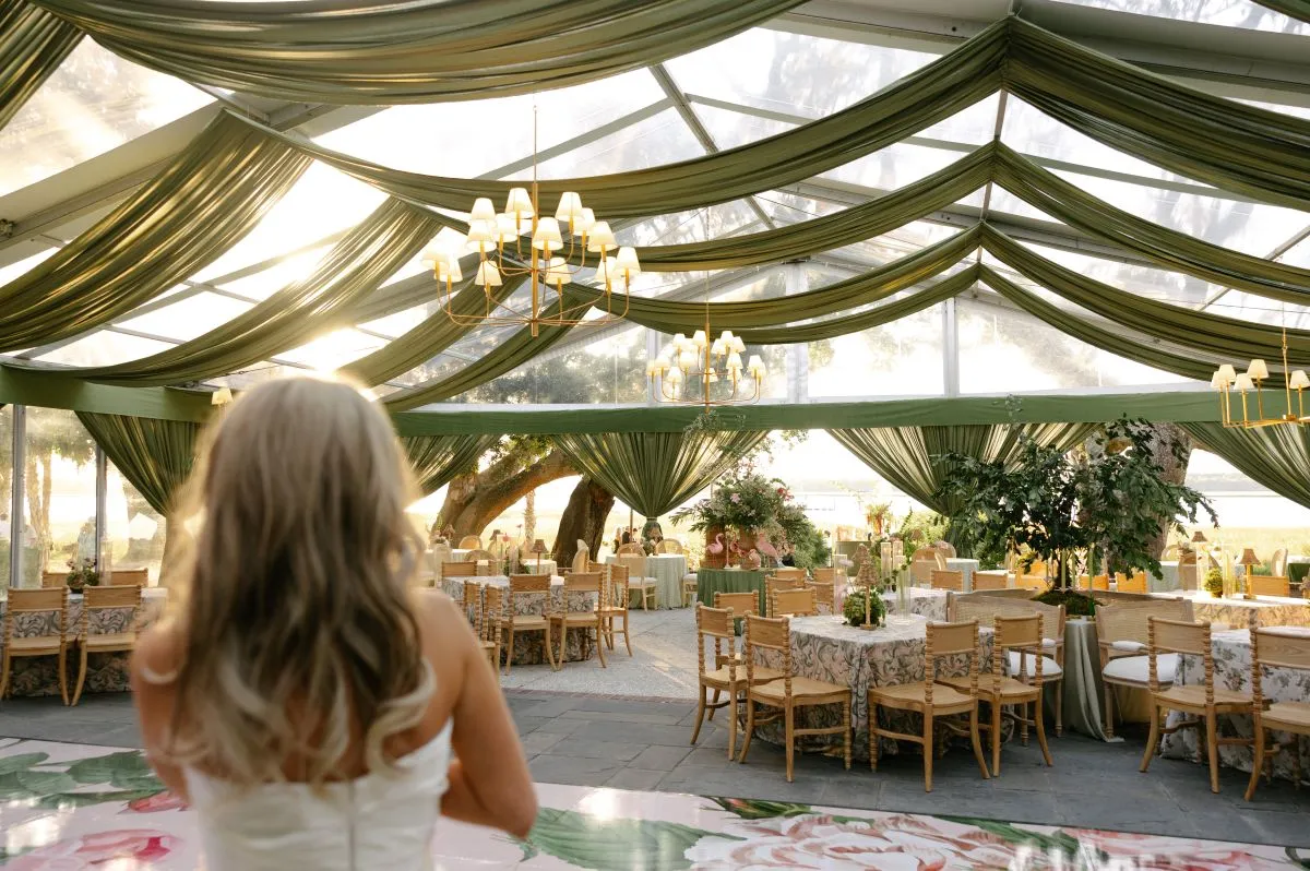 Green-draped clear-top tent with chandeliers and formal dining tables