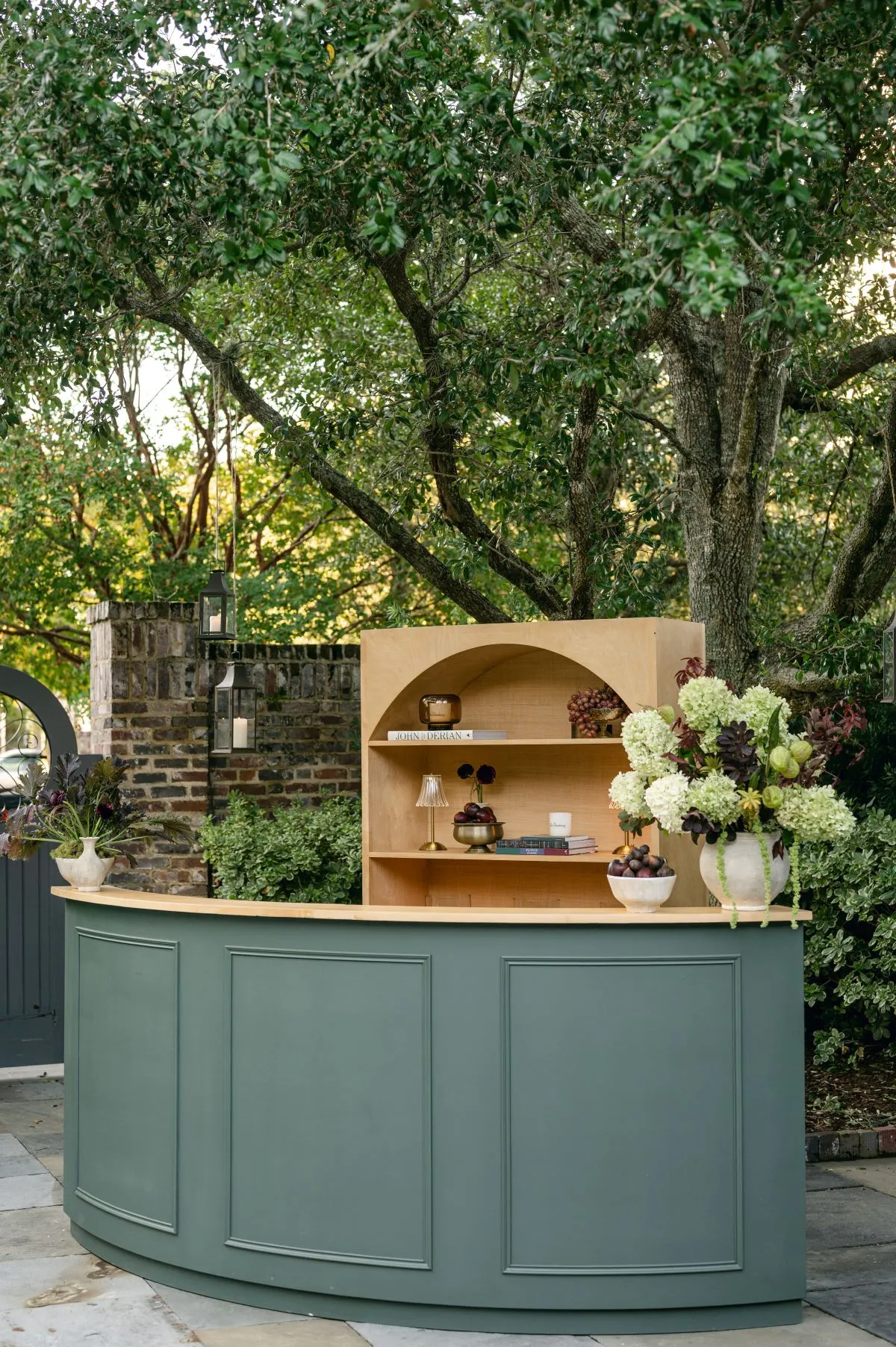 Curved green outdoor bar with wood shelving and white floral arrangement | Curated Events Curved green outdoor bar with wood shelving and white floral arrangement
